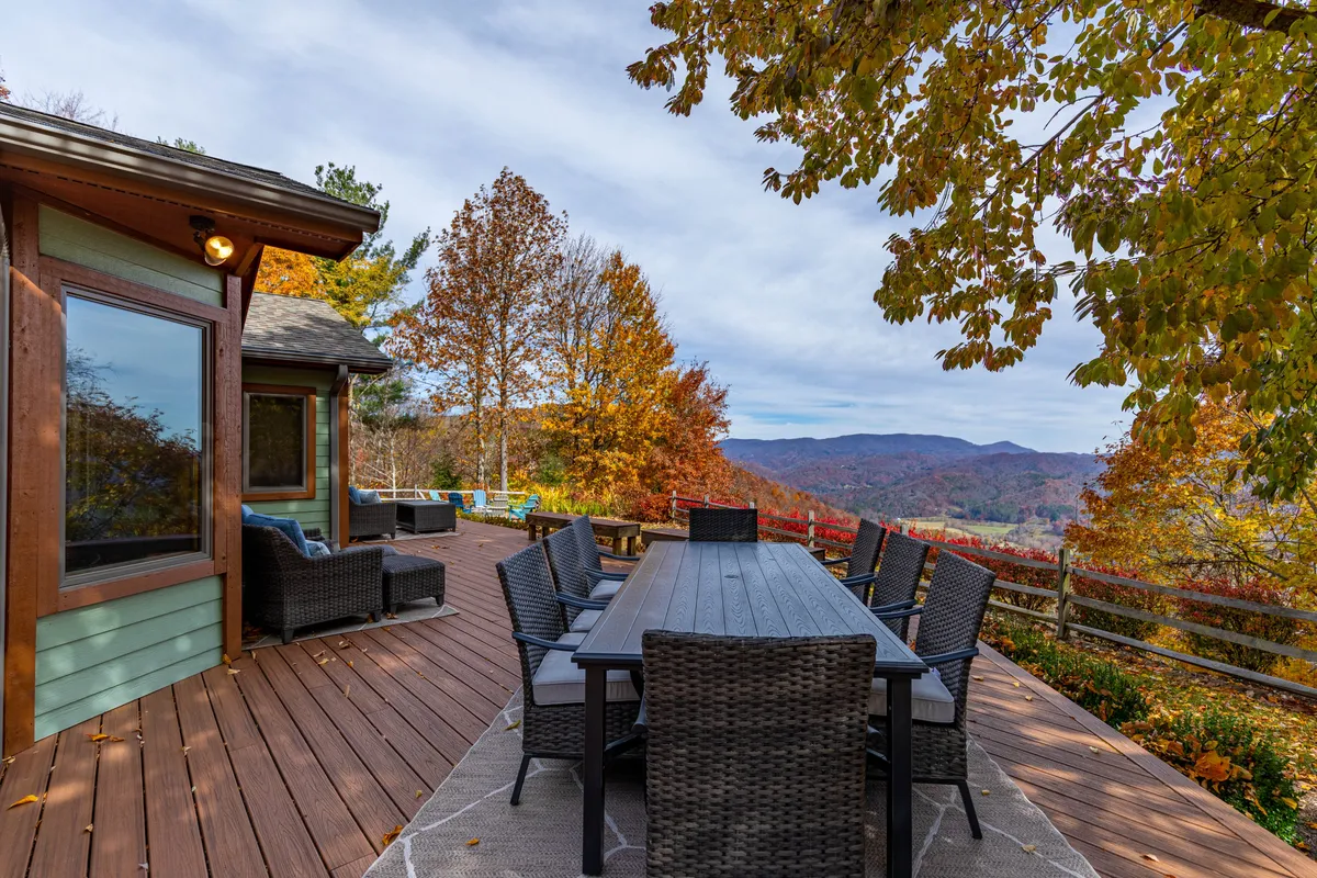 An expansive outdoor dining area with a large table and surrounding chairs overlooks breathtaking mountain vistas and colorful autumn foliage. The setting is ideal for group meals, celebrations, or simply soaking in the natural beauty with friends.