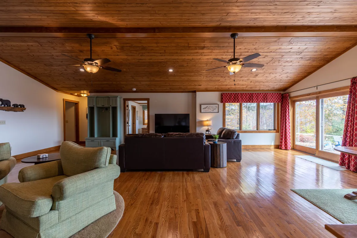 An inviting living space with a wooden ceiling and large windows that frame the outside view. Comfortable seating is arranged for relaxation and socializing, while decorative curtains enhance the cozy, home-away-from-home feeling.