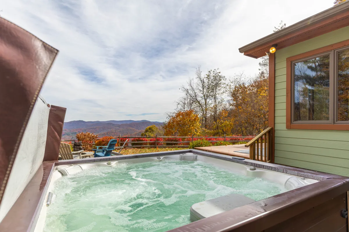 This image displays a bubbling hot tub set on a spacious deck, surrounded by mountain views and autumn foliage. The deck's seating area and the inviting hot tub promise relaxation in all seasons, with the natural beauty of the mountains as a backdrop.