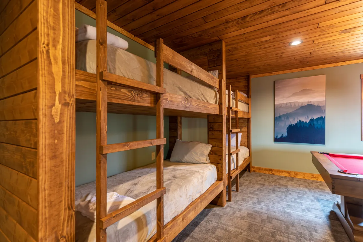 The game room features two sets of XL twin-over-twin bunk beds, mountain-inspired artwork, and a pool table. The space is designed for both sleeping and entertainment, making it ideal for families and groups.