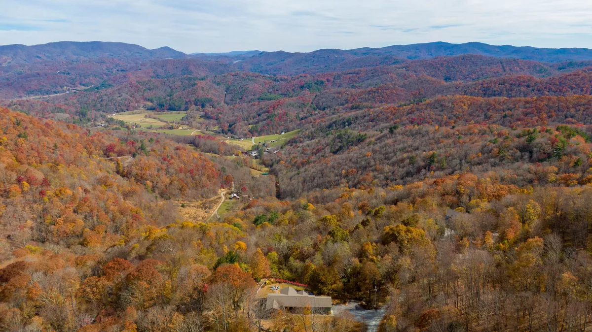 A panoramic view of rolling hills, distant mountains, vibrant autumn foliage, and a quaint village in the valley. The scene evokes a sense of local adventure and the exciting attractions just beyond the lodge.