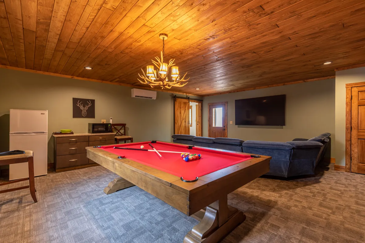 This angle presents the pool table, a comfortable sofa, and the visible refrigerator—part of the wet bar setup. The mood is social and relaxed, highlighting areas for snacking, lounging, and playing.