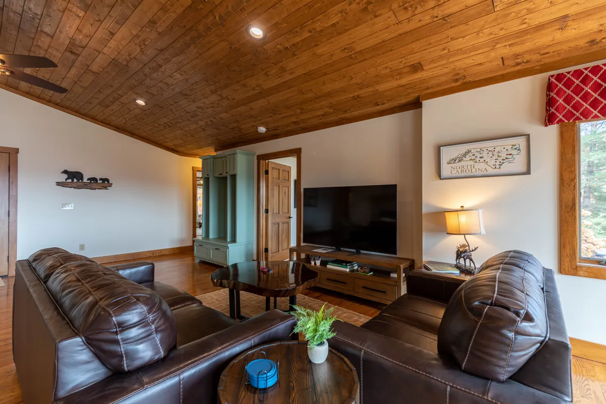 A comfortable living area featuring leather sofas, a wooden coffee table, decorative wall art, a TV, and a window framing scenic views. The arrangement encourages relaxation, conversation, and movie-watching in a welcoming environment.