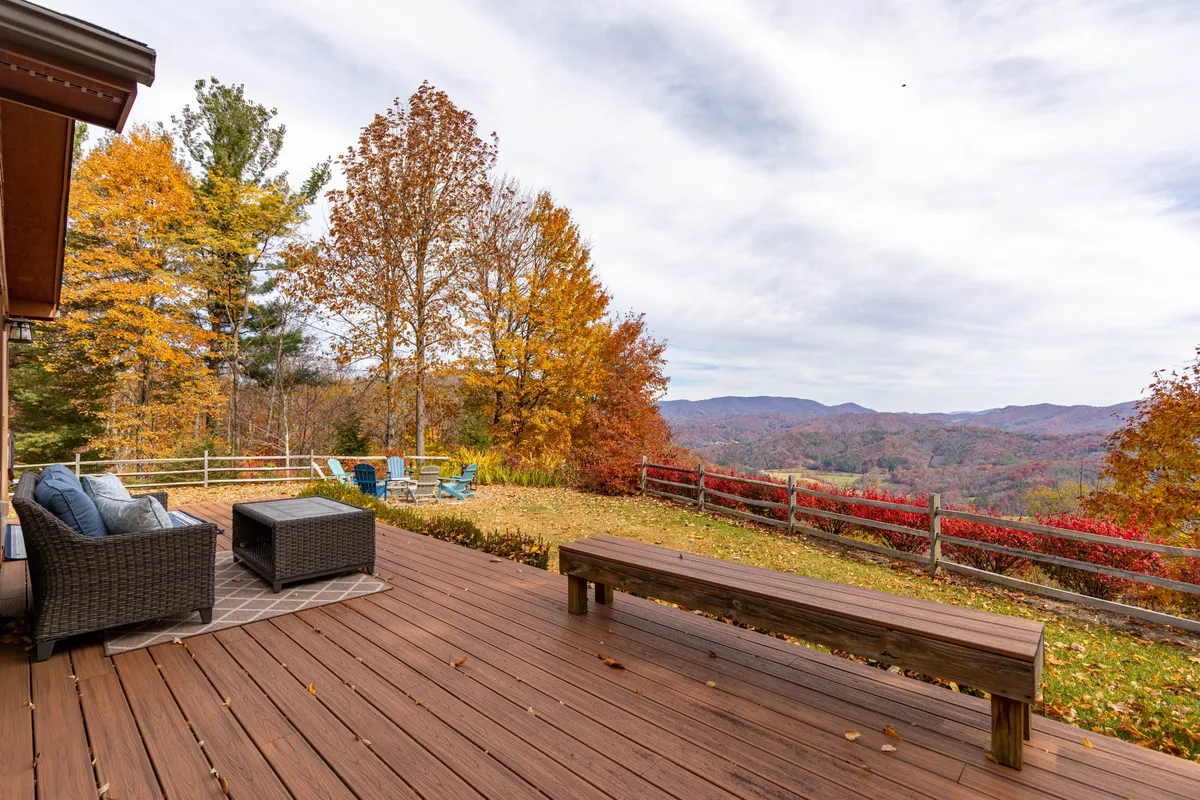 An expansive deck overlooks rolling mountains, with rich autumn colors painting the treetops in the distance. The deck features comfortable outdoor seating, inviting guests to relax and soak in the tranquil views. The scene is open and airy, perfect for both people and pets to enjoy fresh mountain air together.