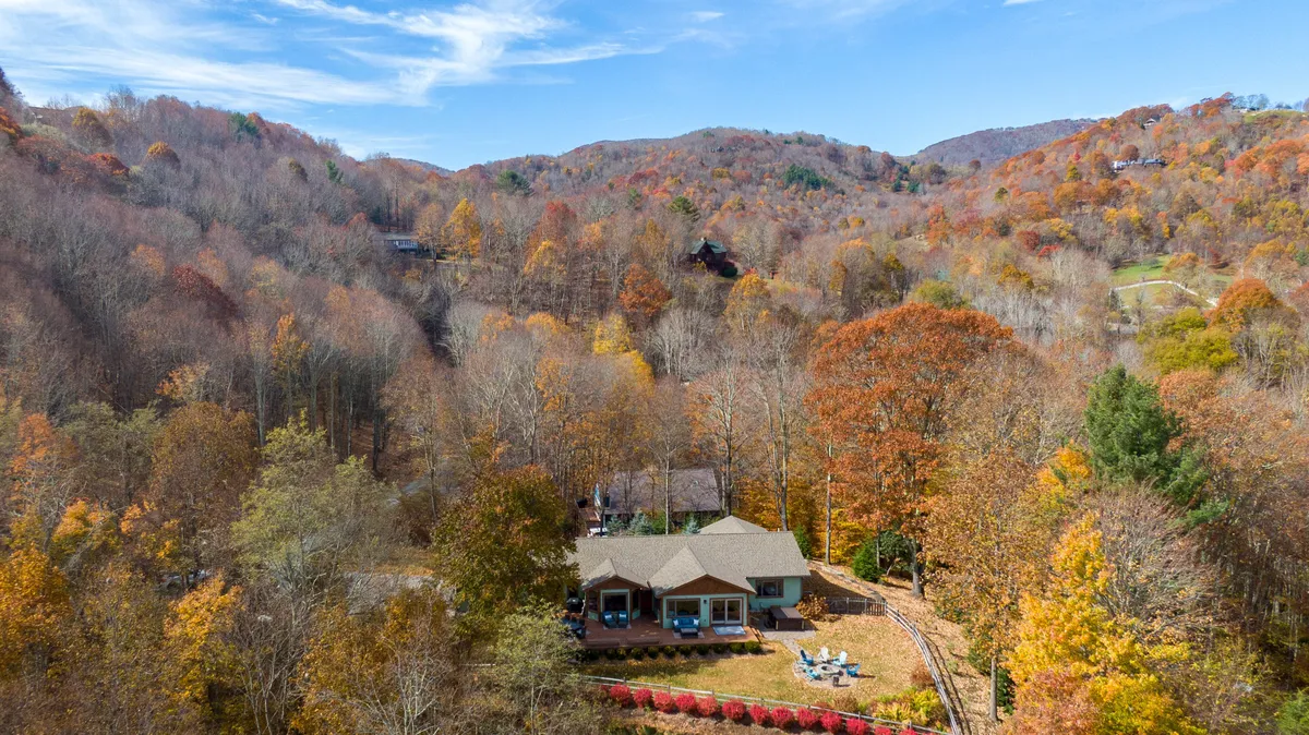 This exterior image features Lookout Lodge surrounded by lush trees, with an inviting outdoor seating area and fire pit. The home’s single-level layout is visible, emphasizing ease of access for all guests. The setting captures the serene mountain landscape that guests can enjoy from outdoor spaces.