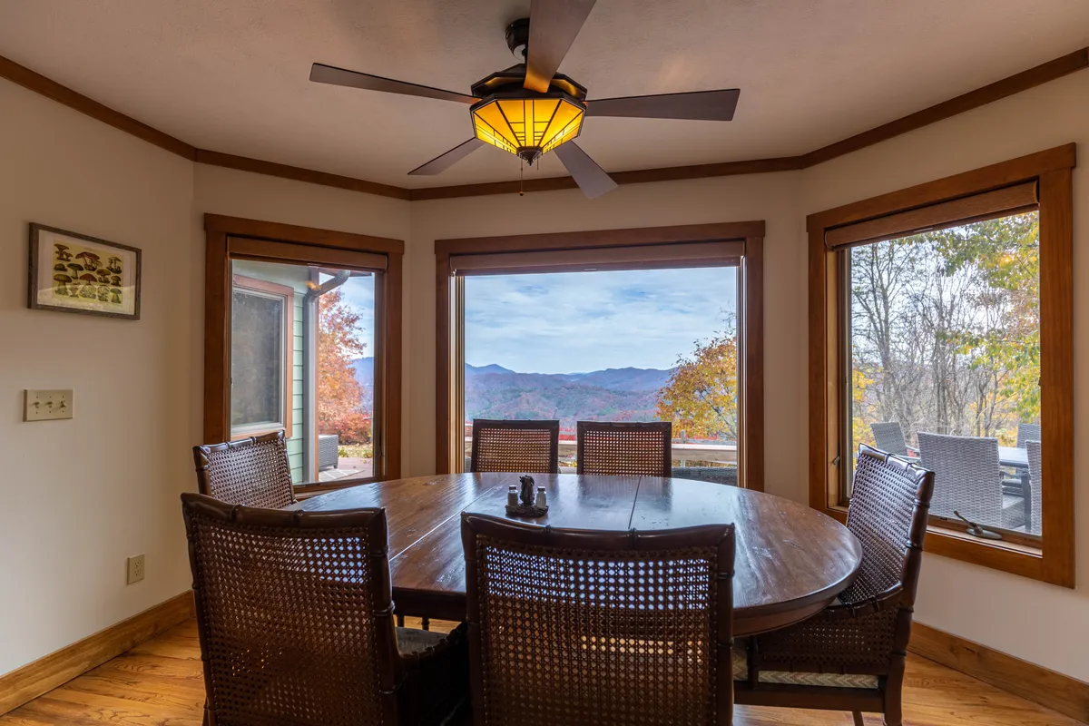 The dining area inside Lookout Lodge features a round wooden table and large windows revealing panoramic mountain views. The space is open and inviting, with wide walkways that underscore its accessible layout.